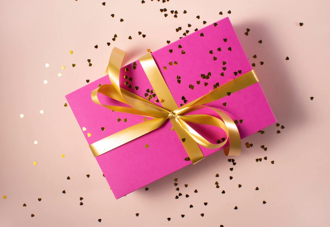 Present with pink paper and tied with a gold bow with glitter sprinkled over.