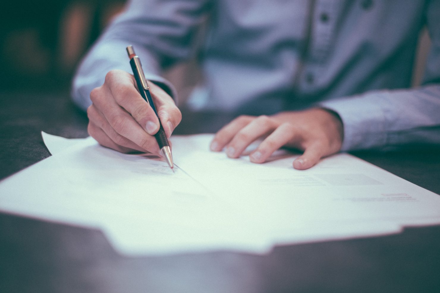 Photo of a man sitting at a desk and writing on paper with a pen.