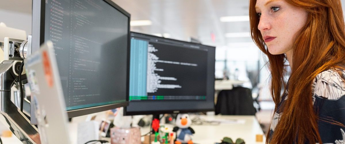 Woman Coding in Office on two Monitors