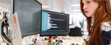 Woman Coding in Office on two Monitors