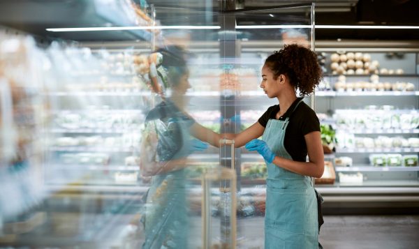 Female retail worker looking into glass refrigerator case with reflection